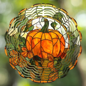 May include: A stained glass pumpkin wind spinner with a swirling, layered design. The pumpkin is orange with a green stem and leaves. The background is a blur of green and brown.