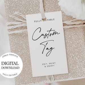 Op de afbeelding: Een cadeau verpakt in glinsterend beige papier met een wit label met de tekst "Custom Tag" in elegant schrift. Het label bevat ook de tekst "Fully Editable" en "Digital Download". Het cadeau is vastgebonden met een beige lint.