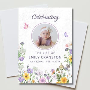 May include: A memorial card with a photo of a baby girl inside a lavender circle, with the text "Celebrating" above. The card is decorated with watercolor flowers and butterflies. The text reads "The Life of Emily Cranston" and dates.