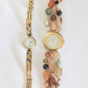 May include: Two vintage women's watches. One has a gold-tone band with geometric accents and a white face. The other watch has a gold-tone face and is surrounded by strands of colorful beads.