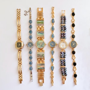 Peut inclure: Une collection de six montres vintage pour femmes avec divers designs. Les montres présentent des bracelets en métal doré et des cadrans de montre de formes carrées, ovales et rondes. Certaines montres ont des accents d'ormeau, de perles et de pierres précieuses.