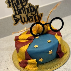 Peut inclure: Un gâteau sur le thème d'Harry Potter bleu et or avec un topper "Happy Birthday Wendy" et une paire de lunettes rondes sur le dessus.