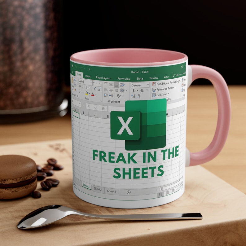 May include: White ceramic mug with a pink interior and handle. The mug features a design resembling a spreadsheet, with the Microsoft Excel logo and the text "FREAK IN THE SHEETS" in green.