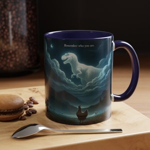 May include: A blue ceramic coffee mug with a white dinosaur silhouette in the clouds and the text "Remember who you are." The mug has a white chicken silhouette in the foreground.