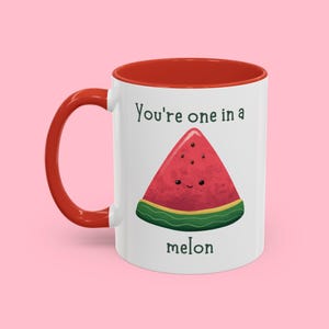 Op de afbeelding: Een witte keramische mok met een rode rand. De mok heeft een watermeloen-afbeelding en de tekst "You're one in a melon".