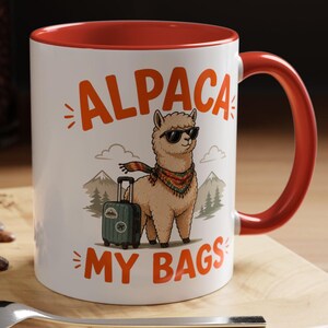 Puede incluir: Taza de cerámica blanca con interior y asa rojos. La taza presenta el texto "ALPACA MY BAGS" en naranja, junto con una ilustración de una alpaca genial con gafas de sol y bufanda, de pie junto a una maleta. La taza está sobre una superficie de madera.