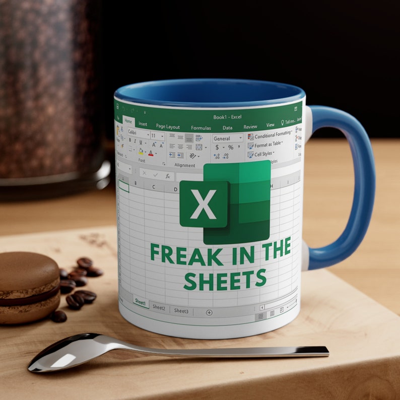 May include: White ceramic mug with a blue interior and handle. The mug features an Excel spreadsheet design with the text "FREAK IN THE SHEETS" in green. The mug is on a wooden surface with a spoon and a pastry.
