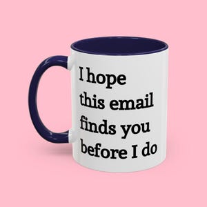 May include: White ceramic mug with a navy blue rim and handle. The mug has black text that reads "I hope this email finds you before I do."