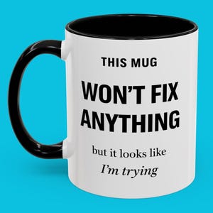 May include: White ceramic mug with a black handle and rim. The mug features the text "THIS MUG WON'T FIX ANYTHING but it looks like I'm trying" in black, bold font. The mug is set against a bright blue background.