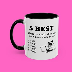 May include: White ceramic mug with a black rim and handle. The mug has a black and white illustration of a cat with a laptop and the text "5 BEST Places to visit when you don't have much money 1. WORK 2. WORK 3. WORK 4. WORK 5. WORK"