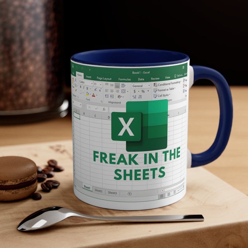 May include: White ceramic mug with a navy blue interior and handle. The mug features an Excel spreadsheet design with the text "FREAK IN THE SHEETS" in green. The mug is on a wooden surface with a spoon and a macaron.