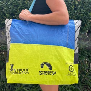 May include: A large tote bag with a blue and yellow color block design. The bag has the text "BOMB PROOF CONSTRUCTION", "Synergy Struts", and "DIRECT STEERING". The bag has a light blue strap.