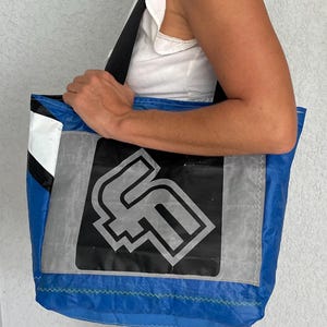 May include: A blue and white tote bag with a black and gray logo featuring the letter "F". The bag has a white stripe and a black stripe on the side.