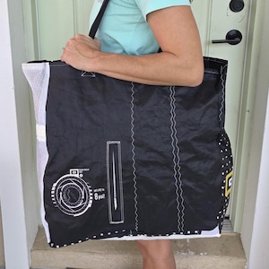 May include: Black tote bag with white accents and a black strap. The bag features white stitching and a graphic with the text "Inflate to 8 psi!". The bag is made of a durable material and is designed for carrying items.