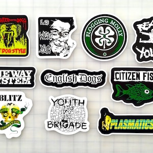 May include: A collection of punk rock and alternative music stickers. Designs include band names like "Slaughter and the Dogs", "Flogging Molly", and "Citizen Fish". The stickers feature bold colors and graphic illustrations.