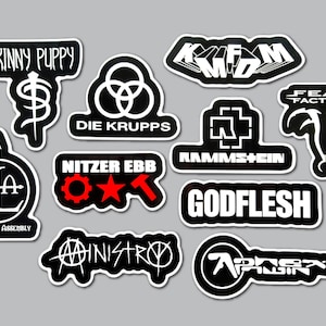 May include: A collection of ten black and white vinyl stickers featuring band logos including Skinny Puppy, KMFDM, Die Krupps, Rammstein, Fear Factory, Front Line Assembly, Nitzer Ebb with red accents, Godflesh, Ministry, and Aphex Twin on a gray background.