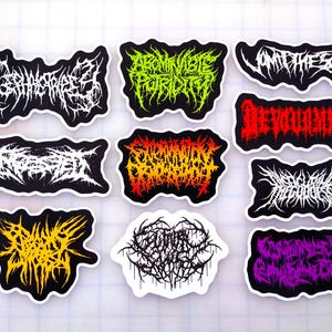 May include: A collection of stickers with black borders and white, yellow, green, orange, and purple text in a gothic font. The stickers feature various words and phrases, likely related to a specific genre or theme.