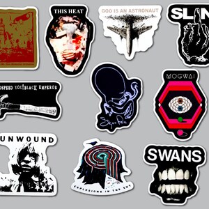 May include: A collection of ten die-cut vinyl stickers featuring various band logos and graphic illustrations, including text such as This Heat, God Is An Astronaut, Slant, Godspeed You! Black Emperor, Sigur Ros, Mogwai, Unwound, and Swans.