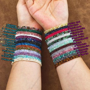 May include: A collection of beaded bracelets in various colors, including rainbow tourmaline, green agate, and amethyst. The bracelets are stacked on wrists, showcasing a variety of gemstones and textures. The image includes text labels identifying each bracelet's stone type.