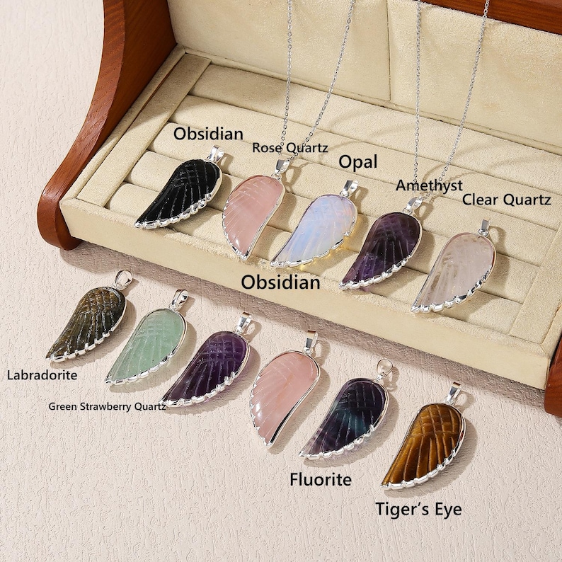 May include: A collection of gemstone wing pendants on silver chains. The pendants are in various colors, including black obsidian, rose quartz, opal, amethyst, and clear quartz. The image also includes Labradorite, Green Strawberry Quartz, Fluorite, and Tiger's Eye pendants.