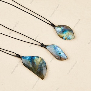 May include: Three labradorite gemstone pendants on black cords. The pendants have a teardrop shape and display iridescent blue, green, and gold hues. The cords are knotted at the top of each pendant.