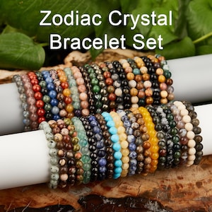 May include: A collection of beaded bracelets in various colors, including red, blue, green, and yellow. The text "Zodiac Crystal Bracelet Set" is displayed at the top. The bracelets are arranged on a white cylindrical surface.