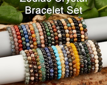 Könnte beinhalten: Eine Sammlung von Armbändern mit Perlen in verschiedenen Farben, darunter Rot, Blau, Grün und Gelb. Der Text "Zodiac Crystal Bracelet Set" ist oben zu sehen. Die Armbänder sind auf einer weißen zylindrischen Oberfläche angeordnet.