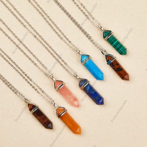 May include: A set of eight silver chain necklaces with crystal point pendants. The pendants are in various colors, including turquoise, pink, orange, brown, blue, and green.