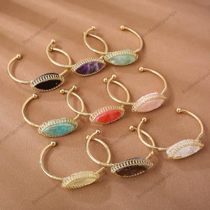 Peut inclure: Une collection de bracelets en métal doré, chacun orné d'une pierre précieuse de couleur différente. Les pierres précieuses comprennent le noir, le violet, le vert, le rouge, le rose et le blanc. Les bracelets ont un design filaire autour des pierres.