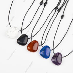 Könnte beinhalten: Fünf Edelstein-Anhänger an schwarzen Schnüren. Die Anhänger sind herzförmig und aus weißen, schwarzen, roten, blauen und violetten Steinen gefertigt.