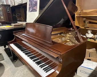 May include: A brown grand piano with the lid open, revealing the ivory keys and black hammers. The piano is in a room with other musical instruments and sheet music.