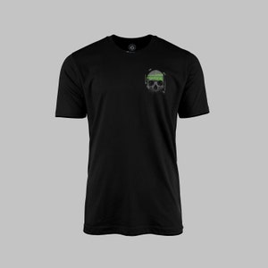 Puede incluir: Camiseta negra con un gráfico de calavera gris en el pecho izquierdo. La calavera tiene una diadema verde con texto similar a código.
