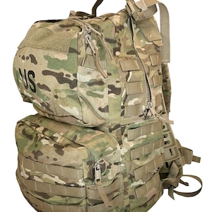 May include: A large, green and brown camouflage backpack with multiple straps and pockets. The backpack has a zippered compartment on the front and a large main compartment. The backpack has a US patch on the front.