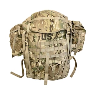 May include: A camouflage-patterned backpack with multiple compartments and straps. The backpack has the letters "US" printed on the front. The bag is designed for carrying gear and supplies.