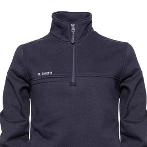 May include: A navy blue sweatshirt with a high collar and a zip-up front. The zipper extends from the collar to the chest. The text "D. SMITH" is embroidered on the left chest. The garment is made of a soft, comfortable material.