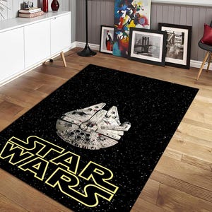 Puede incluir: Alfombra rectangular negra de Star Wars con la nave espacial Millennium Falcon en el centro. Las palabras "STAR WARS" están en letras amarillas en la parte inferior. El fondo es negro con puntos blancos en forma de estrellas.