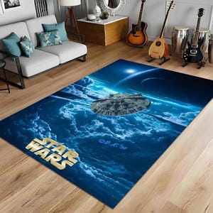 Puede incluir: Una alfombra rectangular de Star Wars con un diseño de nave espacial sobre un fondo de nubes azules y blancas. El logotipo de Star Wars es dorado. La alfombra está sobre un suelo de madera.