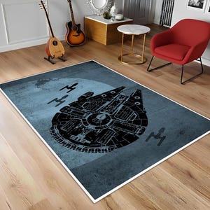 Könnte beinhalten: Rechteckiger Teppich mit einer schwarzen Illustration des Raumschiffs Millennium Falcon auf blauem Hintergrund. Der Teppich enthält auch Illustrationen anderer Raumschiffe. Der Teppich hat einen weißen Rand.