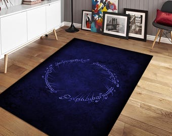 May include: A rectangular, dark blue area rug featuring a circular design with stylized, light blue lettering. The rug has a textured appearance and is placed on a hardwood floor. The design is reminiscent of a fantasy theme.