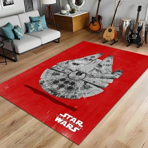 May include: A rectangular red area rug featuring a detailed illustration of the Millennium Falcon starship in shades of gray. The Star Wars logo is printed in white at the bottom, with the text "Los Últimos Jedi" below.