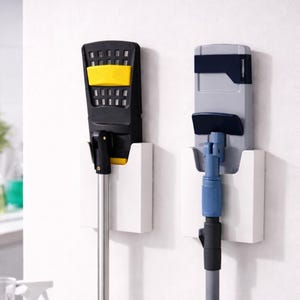 May include: Two wall-mounted mop holders. One is black with yellow accents, the other is gray with blue accents. Both are mounted on white holders. The mops have silver and blue poles.