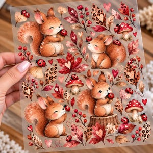 Könnte beinhalten: Ein transparenter Aufkleberbogen mit Illustrationen von braunen Eichhörnchen, roten Pilzen, Marienkäfern und Herbstblättern mit Leopardenmuster und Herzmotiven. Die Designs sind in einem dekorativen Muster auf transparentem Grund angeordnet.