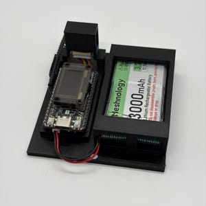 May include: A black 3D-printed housing containing a circuit board with a small rectangular screen and a USB-C port, connected to a 3000mAh Meshnology lithium rechargeable battery. The assembly is mounted on a flat black base with visible wiring.