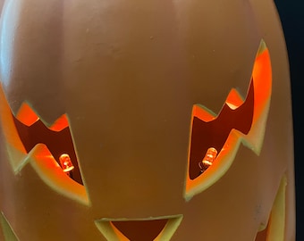 May include: A large orange pumpkin with a carved jack-o'-lantern face. The pumpkin has two lit orange lights inside the eyes.