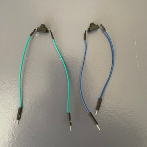 May include: Two black push button switches with blue and teal wires attached to them. The wires have male pin connectors on the ends.