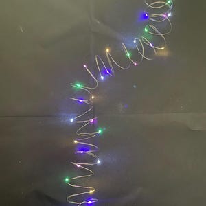 Könnte beinhalten: Eine Lichterkette mit LED-Feenlichtern mit kleinen, farbigen Glühbirnen in Weiß, Grün, Blau, Gelb und Rosa. Die Lichter befinden sich auf einem dünnen, silbernen Draht, der spiralförmig angeordnet ist. Ideal für dekorative Beleuchtung.