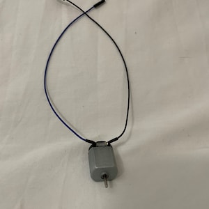 May include: A small silver electric motor with two wires attached. One wire is black and the other is blue.