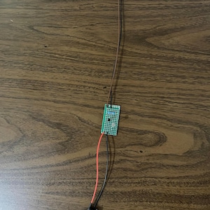 May include: A green circuit board with red and black wires connected to a battery pack and a small LED light.