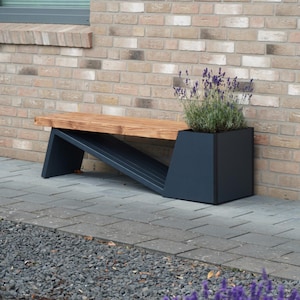 Può includere: Una panchina da giardino con seduta in legno naturale sostenuta da una struttura metallica angolare grigio scuro, che integra un vaso quadrato a un'estremità contenente una pianta di lavanda con fiori viola e foglie verdi.