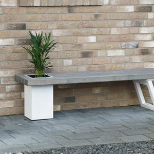 May include: A white wooden bench with a built-in planter, featuring a green plant. The bench is set against a brick wall.